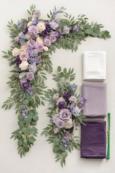 purple flowers and greenery laid out on a white wall next to matching napkins