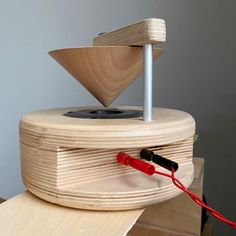 a wooden record player sitting on top of a table next to a red cord and plugged in