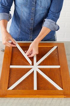 a person is making a wooden cross out of strips of white paper on a piece of wood