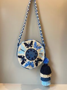 a blue and white basket hanging on the wall next to a tasselled bag