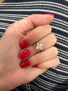 a woman's hand with red nail polish holding a diamond ring