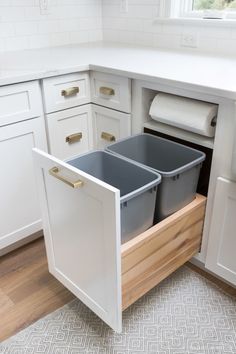 a kitchen with white cabinets and two bins in the bottom drawer, one is open