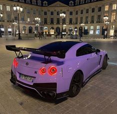 a purple sports car parked in front of a large building at night with its lights on