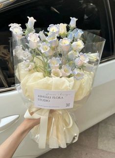 a bouquet of white and blue flowers is being held by someone's hand in front of a car