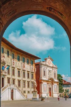 an archway leading to a large building with people walking around in front of it on a sunny day