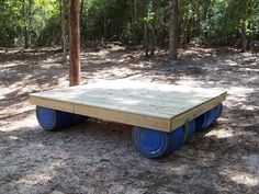 a wooden platform with blue wheels in the middle of some trees and dirt flooring