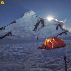 an orange tent pitched up in the snow with a mountain in the background at night