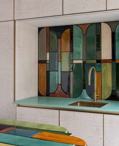 a kitchen sink sitting under a window covered in multicolored glass tiles on the wall