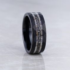 a wedding band with black ceramic and white wood inlays, set on top of a marbled surface