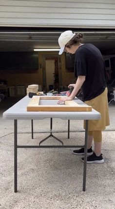 a woman standing at a table with a piece of wood on it