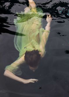 a man floating in the water wearing a green dress and holding his hands up to his chest