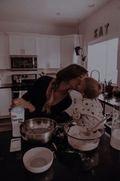 a woman holding a baby in her arms while mixing food on the kitchen counter top