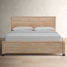 a wooden bed frame with white pillows and sheets on it in a light colored room