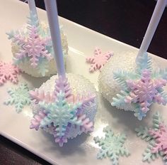 four snowflake cake pops on a white plate with two lit candles in the middle