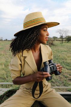 a woman sitting on the back of a truck holding a camera and wearing a hat