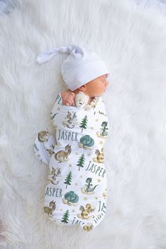 a baby wrapped in a sleeping bag on top of a fluffy white blanket with trees and animals all over it