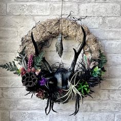 a wreath with antlers, plants and feathers hanging on a brick wall in front of a stone wall