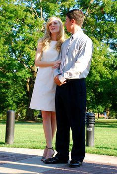 a man and woman standing next to each other on a sidewalk in front of trees