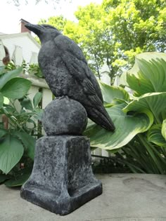 a statue of a bird sitting on top of two rocks in front of some plants