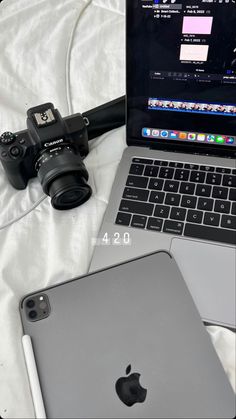 an open laptop computer sitting on top of a bed next to a phone and camera