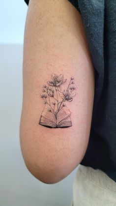 a person with a tattoo on their arm holding an open book and flowers in it