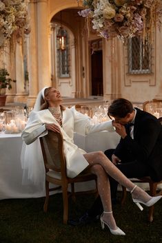 a man and woman sitting at a table in front of a chandelier with candles