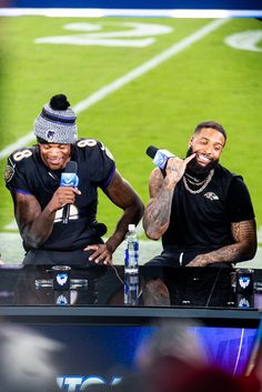 two football players sitting at a table with microphones in their hands and one holding a cell phone to his ear