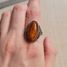 This is a vintage sterling silver ring, with a long oval amber cabochon that has exquisite Baltic amber full of inclusions. The setting is decorated with scroll and bead elements on the edges where it meets the band. It is marked 925 and sized at 8.75. The ring is in good vintage condition with expected patina and wear. Oval Amber Cabochon Jewelry, Hallmarked Amber Oval Cabochon Jewelry, Classic Amber Oval Cabochon Jewelry, Heirloom Amber Oval Jewelry, Heirloom Oval Amber Jewelry, Classic Amber Cabochon Jewelry, Antique Amber Cabochon Rings, Handmade Amber Oval Cabochon Rings, Vintage Baltic Amber Jewelry For Formal Occasions