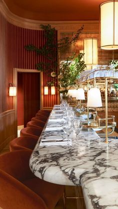 a long marble table with chairs and lamps on it in front of a bar area