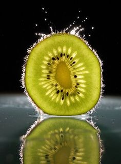 a kiwi fruit sliced in half with water splashing on it's surface