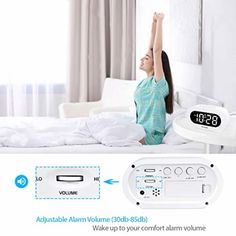 the alarm clock is on display in front of a woman sitting on a bed with her arms up