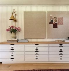 a white dresser with lots of drawers next to a lamp and flowers on the table