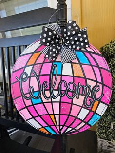 a pink and black welcome sign with polka dots on the top, hanging from a lamp post