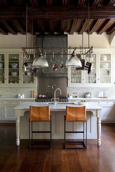 a kitchen with wooden floors and hanging lights above the island, along with two brown leather chairs