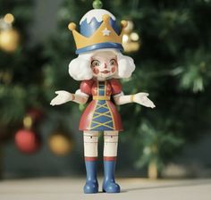 a toy figurine with a crown on it's head stands in front of a christmas tree