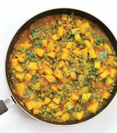 a pan filled with vegetables and peas on top of a white table next to a spatula