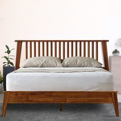 a wooden bed frame with two pillows on it and a plant in the corner next to it