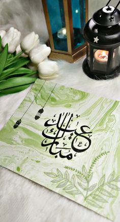 an arabic calligraphy is displayed on a table next to some flowers and a lantern