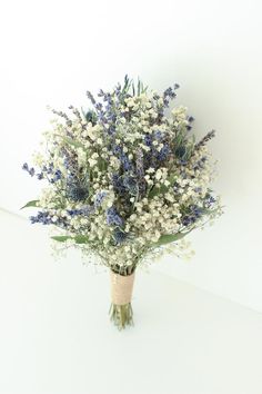 a bouquet of blue and white flowers in a vase on a table with a white wall behind it