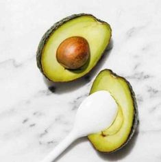 an avocado is cut in half with a spoon next to it on a marble surface