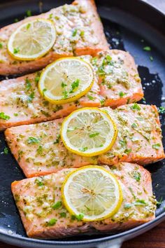 four pieces of salmon with lemons and chives on a black plate, ready to be cooked