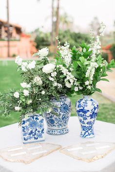 three blue and white vases sitting on top of a table with flowers in them