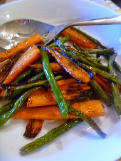 a white plate topped with carrots and asparagus next to a silver spoon