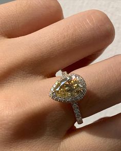 a close up of a person's hand holding an engagement ring with a yellow diamond