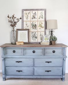 a blue dresser with flowers and pictures on the wall above it, along with a lamp