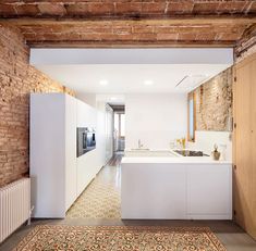 an open kitchen and living room area with brick walls, exposed ceilinging, and white cabinets