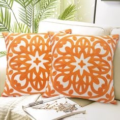 two orange and white pillows sitting on top of a couch next to a plant in a vase