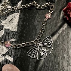 a close up of a chain with a butterfly on it and a pink stone next to it