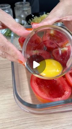 two hands are squeezing an egg into tomatoes in a glass bowl on a wooden table