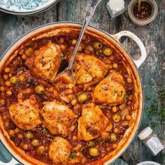 a pot filled with chicken and olives on top of a wooden table